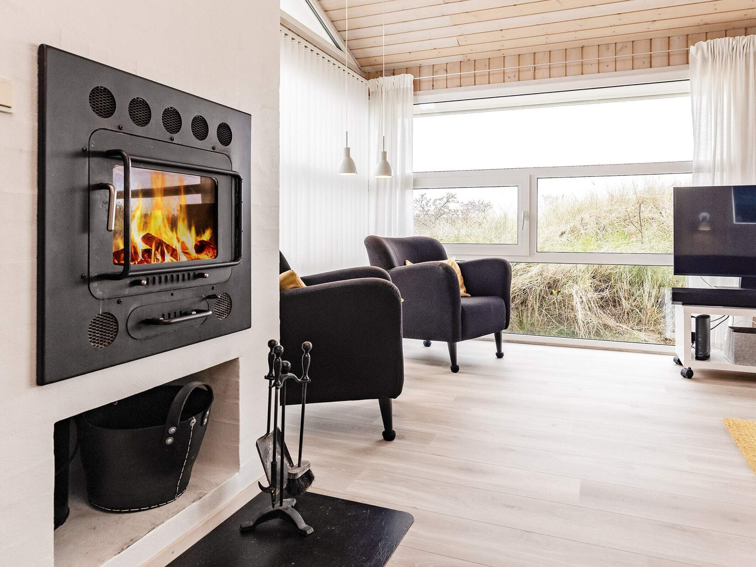 A modern living room with a fireplace, two armchairs, a television, and a large window with a view of the outdoors.