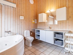 Une salle de bain aux murs lambrissés, dotée d’une baignoire sur pieds, de toilettes, d’un lavabo avec un miroir et de paniers de rangement.