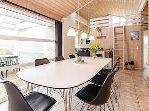 Uma área de refeições moderna com uma mesa grande branca, cadeiras pretas e iluminação pendente.