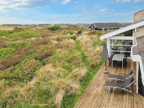 A wooden deck with outdoor furniture, overlooking a dune landscape with vegetation.