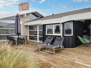 A modern outdoor patio with a wooden deck, a table with chairs, and two lounge chairs.