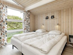 A bedroom with a wooden ceiling, a bed with white bedding, two bedside tables, and a window with curtains.