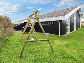 A wooden swing set in a grassy area with a modern building in the background.
