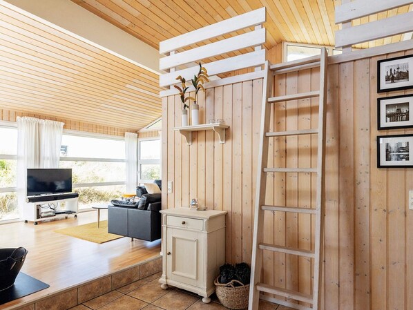 Un salon chaleureux avec un plafond en bois, un canapé noir, un téléviseur et un meuble blanc.