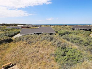 A coastal area with multiple buildings, some with flat roofs and others with sloped roofs, surrounded by dry grass and shrubs. - 5 Star Holiday Home in Hjorring (Hjørring)