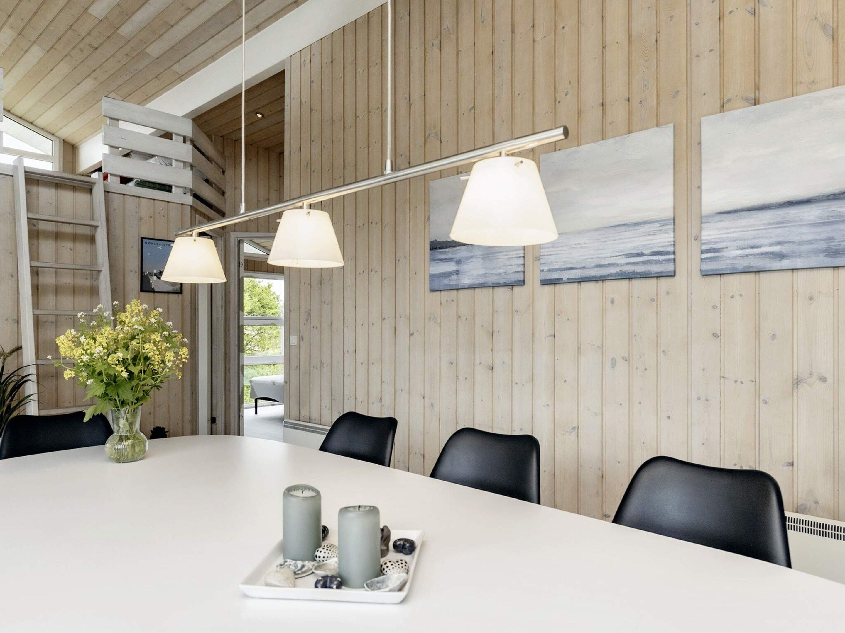 A modern dining area with a long table, chairs, and a vase of flowers.