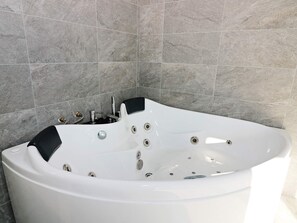 A modern bathroom with a freestanding jacuzzi tub, a handheld showerhead, and a built-in faucet.