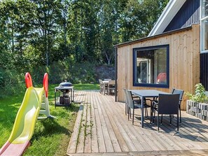 A wooden deck with a table and chairs, a slide, and a barbecue grill. - 5 Star Holiday Home in Hadsund (Hadsund)