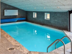 An indoor swimming pool with a clear blue water, a blue poolside area, and a ceiling with recessed lighting.