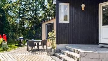 En hyggelig, mørk træhytte med terrasse og udendørs siddeplads.