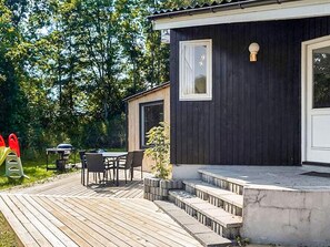 A small, dark wooden cabin with a deck and outdoor seating area.