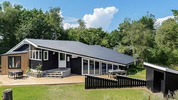 Et moderne hus med stor terrasse, overdækket patio og en indhegnet have.