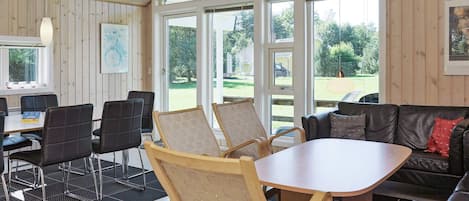Ein Zimmer mit Holzvertäfelung, einem runden Tisch und einer Couch. Stühle sind um den Tisch herumgestellt und ein Fenster bietet Blick auf Grünfläche.