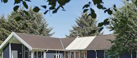 A two-story building with a sloped roof, a covered patio area with outdoor seating, and a grassy lawn.