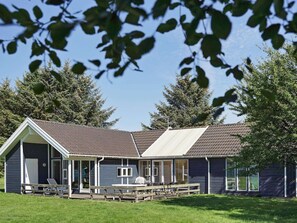 A two-story building with a sloped roof, a covered patio area with outdoor seating, and a grassy lawn.