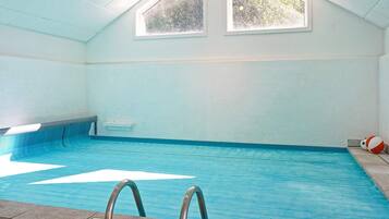 An indoor swimming pool with clear blue water, a tiled floor, and a roof with skylights.