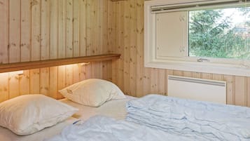 Ein Zimmer mit Holzwänden, einem Bett, Kissen, einem Fenster und einem Regal.