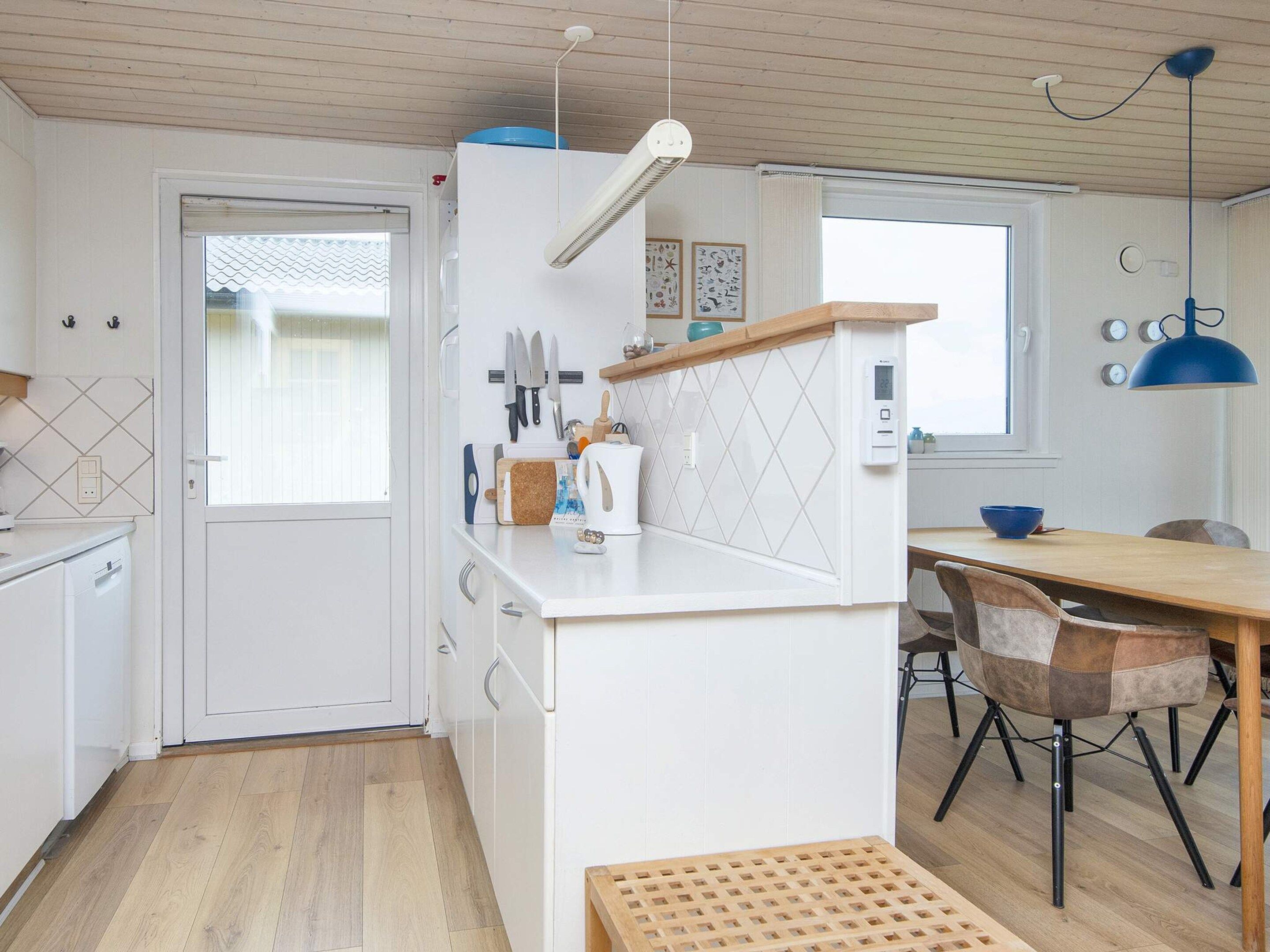 A compact kitchen with white cabinetry, a wooden dining table, and a blue pendant light.