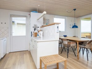 A modern kitchen with white cabinetry, a wooden dining table, and a bench. - 5 Person Holiday Home in Lemvig (Lemvig)