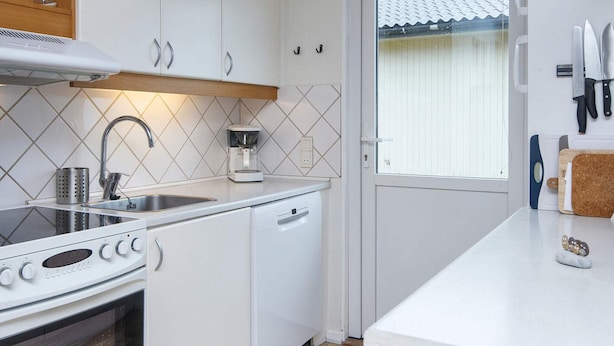 A kitchen with white cabinets, a stainless steel sink, a coffee maker, and a window with blinds. - 5 Person Holiday Home in Lemvig (Lemvig)