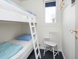 Habitación con literas, una escalera, una silla blanca, una ventana con persianas y una puerta con pomo de latón.