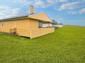 A single-story building with a flat roof, a wooden deck, and a grassy field in the background. - 5 Person Holiday Home in Lemvig (Lemvig)