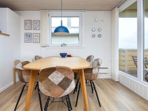 A dining area with a round table, six chairs, a blue pendant light, and a window with a view.