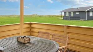 A covered outdoor seating area with a table and chairs, overlooking a grassy field and a house. - 5 Person Holiday Home in Lemvig (Lemvig)
