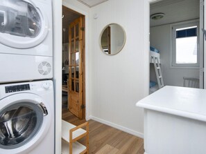 A laundry room with a washing machine, a drying rack, and a wooden door leading to another room.