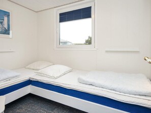 Et enkeltværelse med et vindue, hvide vægge og en blå detalje ved sengebunden.
