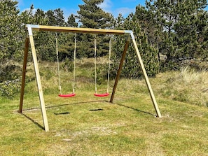 Eine Holz-Schaukel mit zwei roten Sitzen in einer grünen Wiese, im Hintergrund Bäume.