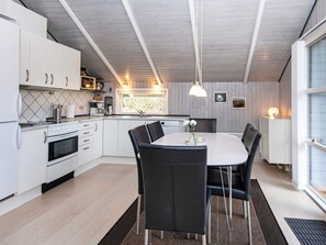 A modern kitchen with white cabinets, a dining table with chairs, and a window with natural light. - 4 Star Holiday Home in Blavand (Blavand)