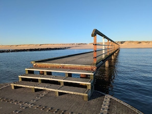 A wooden pier extending into calm water with a metal railing and steps leading to the water's edge.