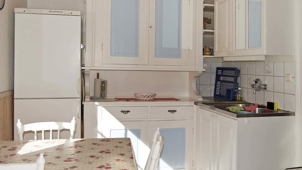 A compact kitchen with white cabinets, a dining table with a floral tablecloth, and a small refrigerator.