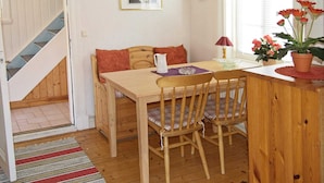 A cozy dining area with a wooden table and chairs, a small window with flowers, and a staircase leading to another room.