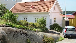 A white house with a red-tiled roof, a stone wall, and a car parked in front.