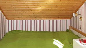 A room with a wooden ceiling, a bed with a green bedspread, a white dresser, and striped wallpaper.