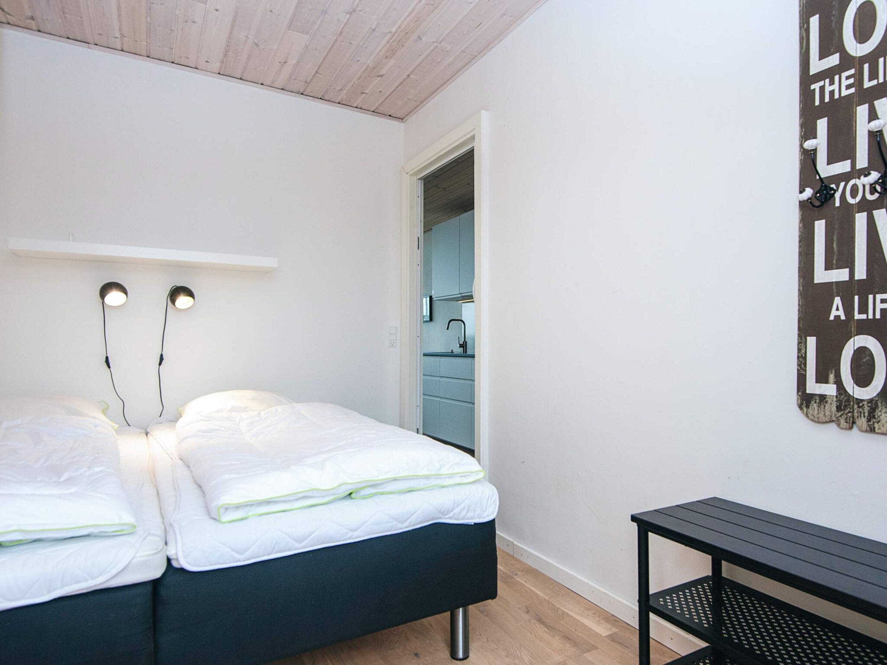 A bedroom with two beds, a nightstand, and a wall-mounted light fixture.