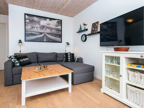 En stue med en grå sofa, et træbord, et fjernsyn og et skab med glas.