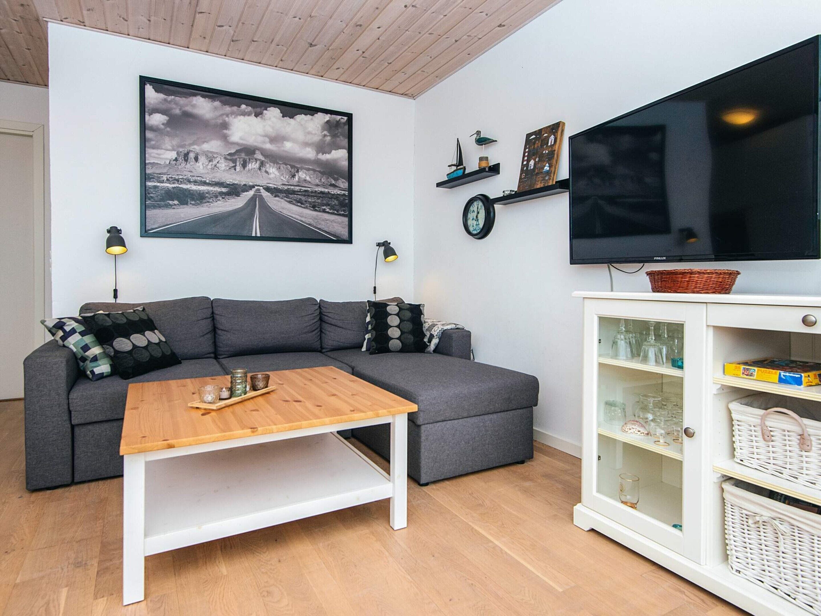 A living room with a grey sofa, a wooden coffee table, a television, and a cabinet with glassware.