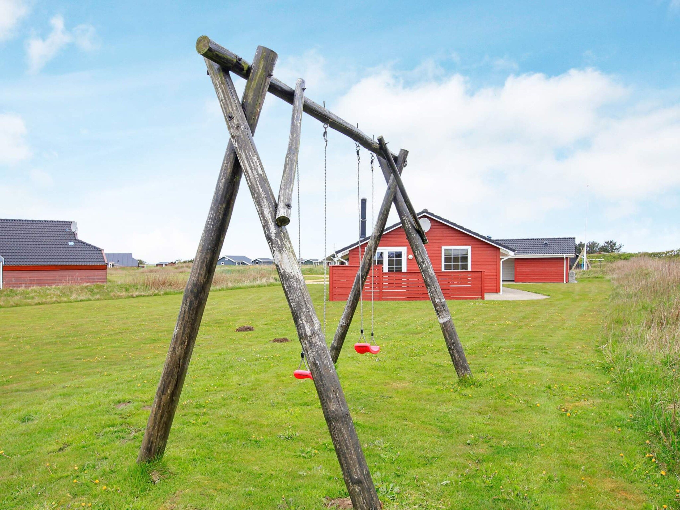 A swing set in a grassy field with a red building in the background.