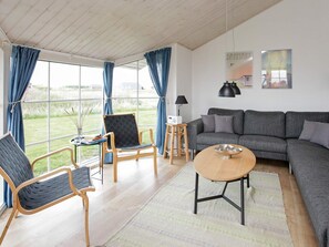 A modern living room with a grey sofa, two armchairs, a coffee table, and a large window with curtains.