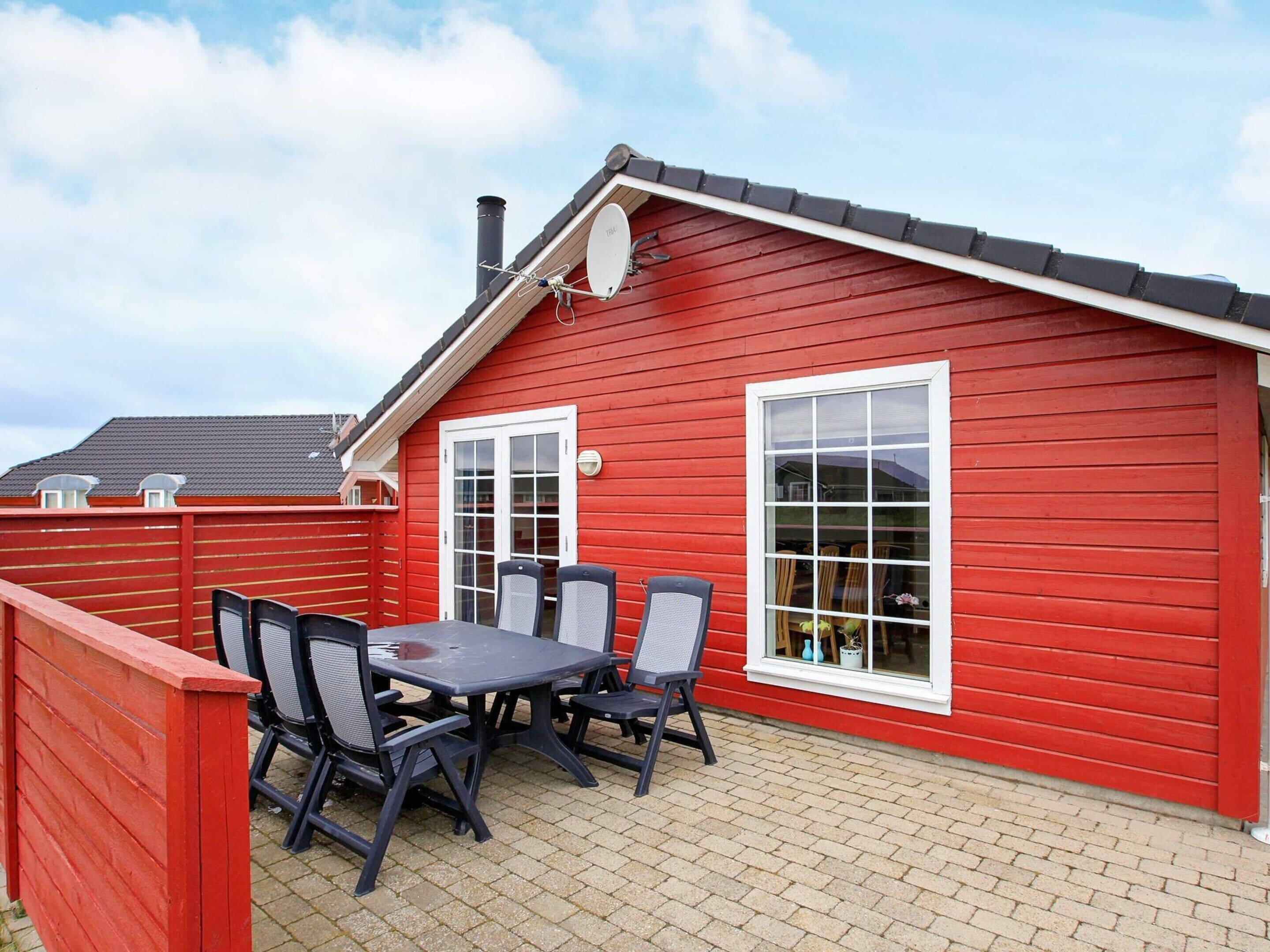 A red wooden building with a tiled patio, a table with chairs, and a satellite dish.