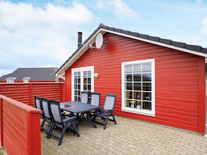 A red wooden building with a tiled patio, a table with chairs, and a satellite dish. - Picturesque Holiday Home in LÃ¸kken near Sea (Lokken)