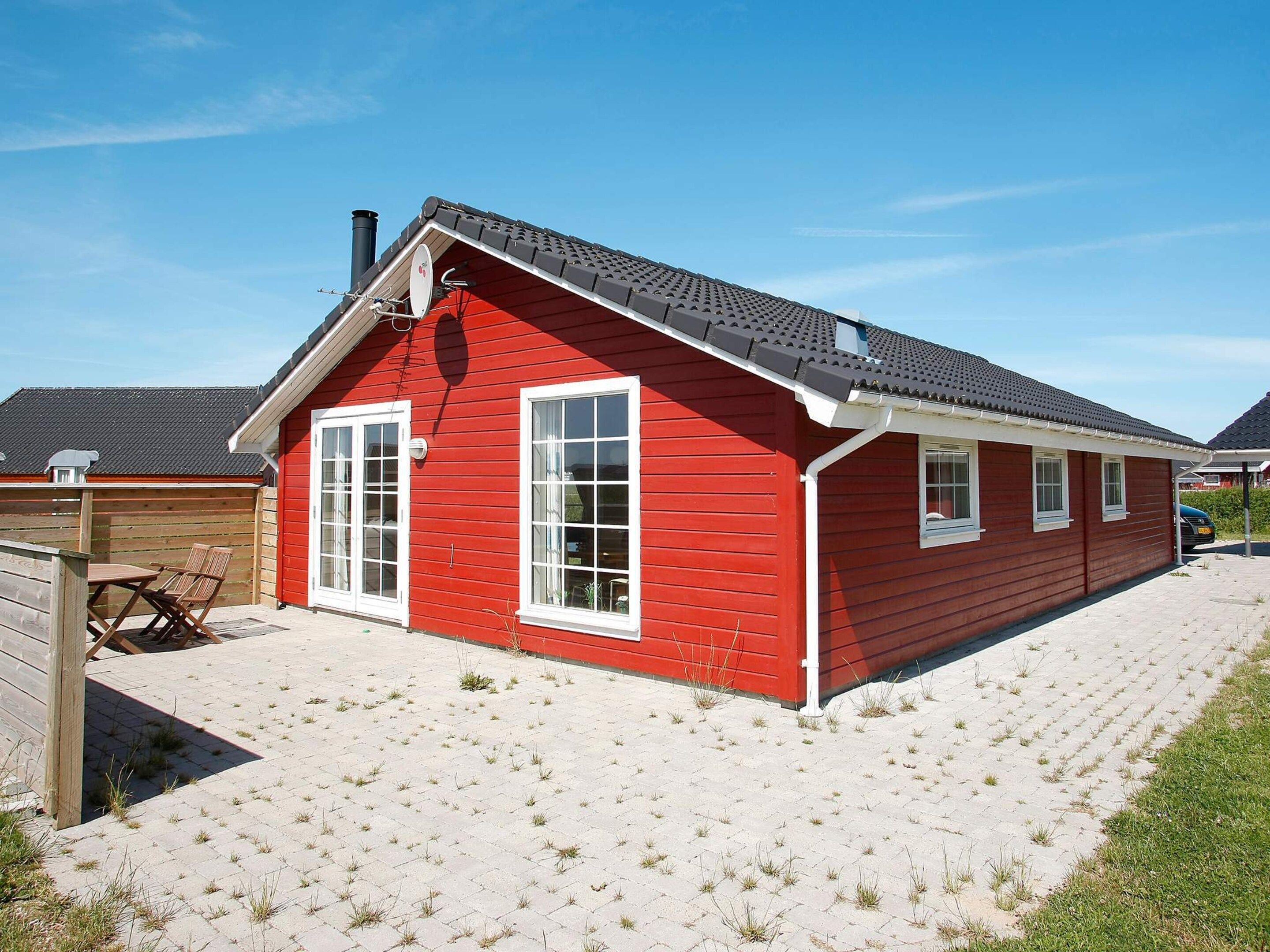 A red wooden house with a sloped roof, white windows, and a chimney.