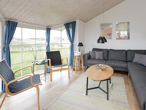 Una sala de estar moderna con un sofá gris, dos sillones, una mesa de centro y un ventanal con cortinas.