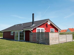 Ett rött hus med en svart skorsten, ett trästaket och en klarblå himmel.