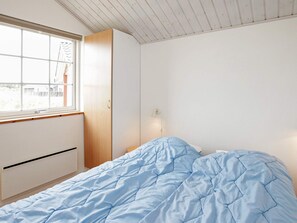 Un dormitorio con cama, armario, ventana y lámpara de pared.