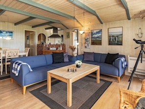 A cozy living room with a blue sofa, a wooden coffee table, and a dining area with a table and chairs. - 5 Star Holiday Home in Oster Assels (Øster Assels)