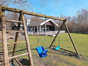 A wooden swing set with two swings and a ladder, set against a backdrop of a house and a grassy field. - 5 Star Holiday Home in Oster Assels (Øster Assels)